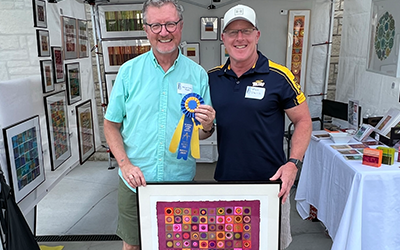 Steven Tozer Wipfli holding his Purchase Award ribbion in front of his Art on The Mall booth