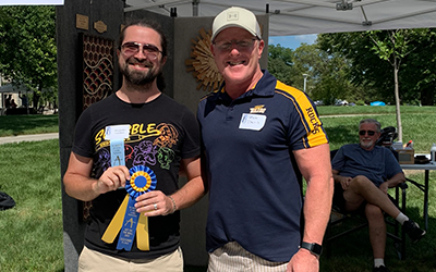 Alexander Gardner holding his second palce ribbion in front of his Art on The Mall booth