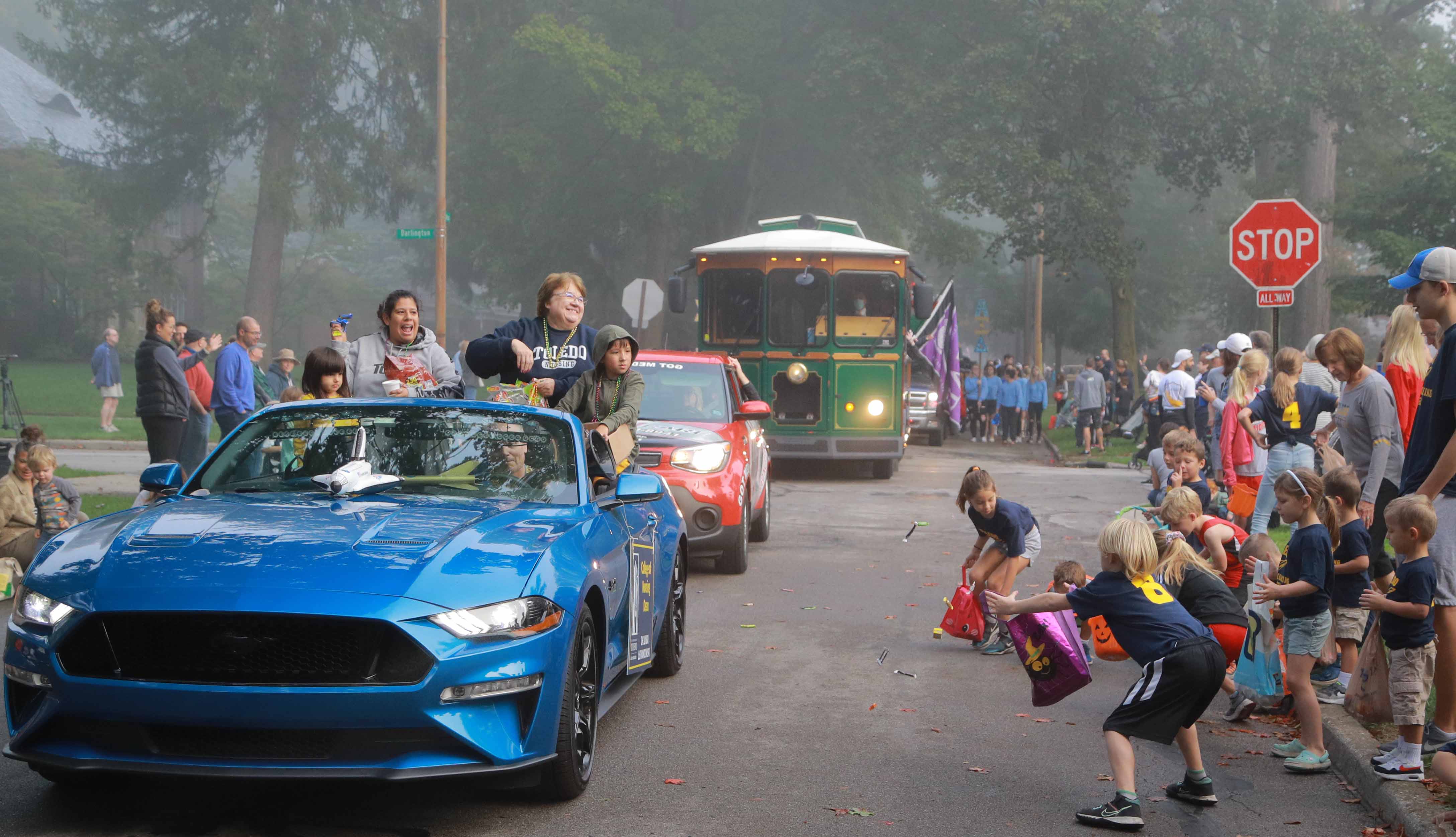 College of Nursing dean in a blue Ford mustang throwing candy to children on sidewalk during 2021 homecoming parade