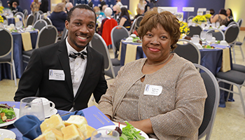 Two smiling alumni sitting at Homecoming gala table