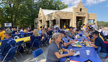 alumni sitting at rows of tables eating and talking at the Koester alumni pavilion during the pregame party