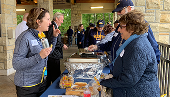 Two alumni working the pregame party hot dog buffet and passing out ingredients to a guest in line