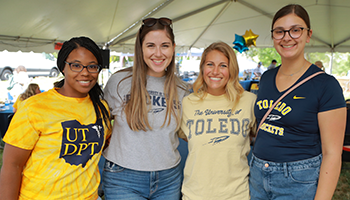 Four female UToledo students at an outdoor football event smiling at the camera